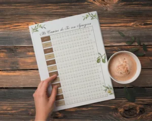 Planificador anual de lectura bíblica titulado "Mi Camino de Fe con Spurgeon" sobre mesa de madera, con una taza de café y ramas de olivo decorativas.