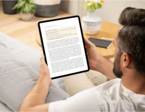 Mockup de un hombre leyendo un libro cristiano en formato digital en una tablet, sentado en un sofá cómodo con un fondo hogareño y cálido.