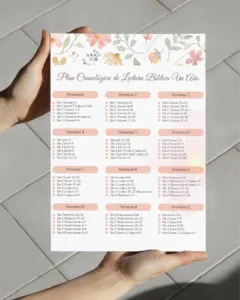 Manos sosteniendo impresión de plan cronológico de lectura bíblica en PDF con flores en rosa pastel sobre piso de losetas.