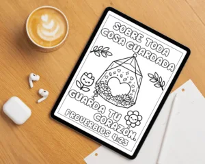 Página para colorear de Proverbios 4:23 en una tableta digital sobre escritorio de madera junto a una taza de café, audífonos y libreta de notas.